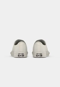 Baskets blanches en toile avec un design bas, une tige texturée et un logo noir "Converse All Star" sur le talon. Semelle blanche uni.