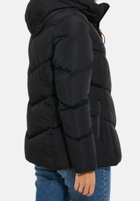 Veste matelassée noire avec capuche, dotée d'une isolation matelassée, d'une poche zippée latérale et de poignets élastiques. Texture lisse et coupe régulière.