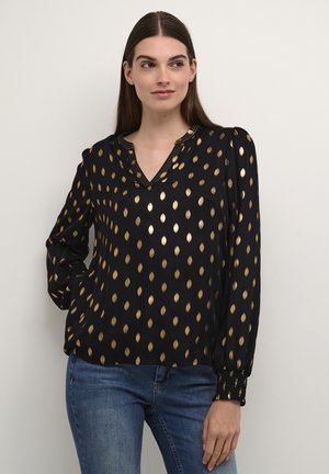 Svart blus med mönster av guldblad, långa ärmar, V-ringning, puffärmar med veck och elastiska manschetter. Kombinerad med denimjeans.