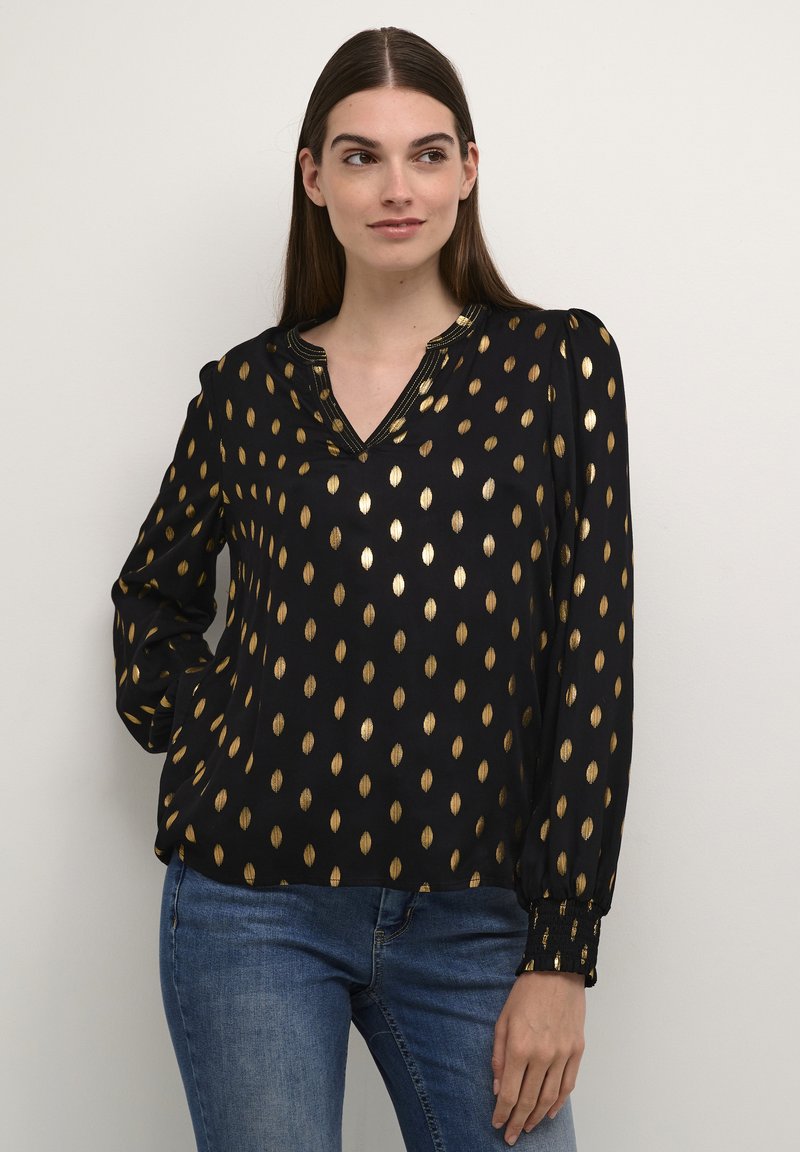 Blusa nera con motivi a foglia dorata, maniche lunghe, scollatura a V, spalle a palloncino arricciate e polsini elastici. Abbinata a jeans in denim.