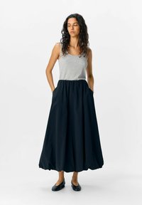 Falda negra larga en forma de A con cinturilla fruncida y bolsillos laterales, combinada con una camiseta ajustada gris; tejido suave, diseño minimalista.