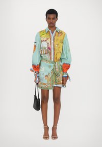 Rochie cămașă colorată, cu modele în verde mentă și galben, având mâneci lungi, talie legată și ilustrații intricate. Material ușor.
