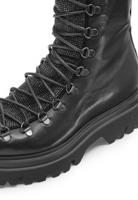 Stivale in pelle nera con pannello in rete testurizzata, design con lacci e accessori metallici, e una suola spessa e robusta per una buona aderenza.