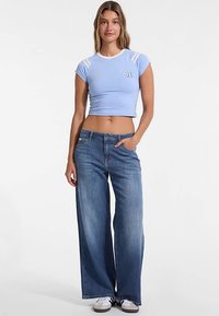 Tricou albastru deschis scurt, cu accente albe și numărul "81" imprimat, asortat cu blugi albaștri largi și adidași albi.