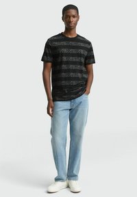 Zwarte t-shirt met korte mouwen en een gestructureerd gestreept patroon. Gecombineerd met lichtblauwe jeans en witte sneakers, wat een casual look creëert.