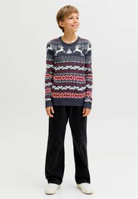 Kötött pulóver sötétkék alappal, fehér rénszarvas mintákkal, valamint piros és fehér geometriai mintákkal. Fekete, bő szabású nadrággal párosítva.