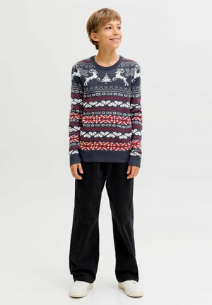 Maglione lavorato a maglia con una base blu scuro, motivi di renne bianchi e disegni geometrici rossi e bianchi. Abbinato a pantaloni neri a gamba larga.