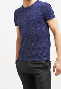 Camiseta de manga corta en azul marino con un patrón geométrico. Hecha de una tela texturizada, presenta un cuello redondo y una pequeña etiqueta de logo en el dobladillo.