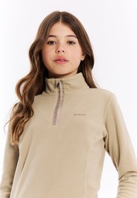Beige fleece trui met een hoge kraag en een halve rits. Heeft een contrasterende rits en een geborduurd logo op de borst.