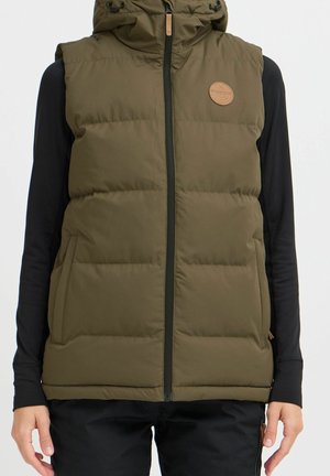 Olivengrøn polstret vest med lynlås foran og hætte, båret over sort langærmet trøje og sorte bukser, nærbillede af overkroppen.