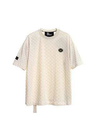 Camiseta de manga corta texturizada en color crema con patrón a cuadros, pequeño logo circular negro y dorado en el pecho, detalle de raya negra en la manga izquierda.