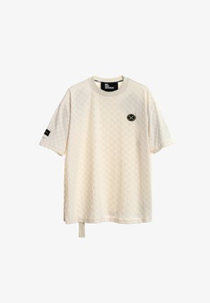 Camiseta de manga corta texturizada en color crema con patrón a cuadros, pequeño logo circular negro y dorado en el pecho, detalle de raya negra en la manga izquierda.