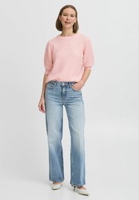 Roze, ribbelgebreide trui met korte mouwen, gecombineerd met lichtblauwe, wijde jeans en witte hakken. Eenvoudig ontwerp en minimale details.