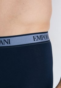 Námorné bavlnené spodné prádlo s svetlomodrým elastickým pásom s nápisom "EMPORIO ARMANI" v čiernom písmene. Hladká textura, priliehavý strih.