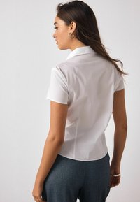 Biela košeľa s krátkym rukávom a golierom, hladká textúra, priliehavý strih, bez viditeľných vzorov alebo ozdôb.