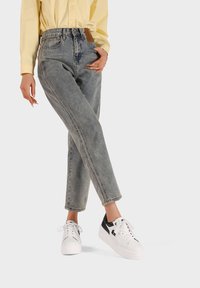 Jeans grigi chiari a vita alta con un design a gamba dritta e una texture scolorita, abbinati a sneaker bianche con dettagli neri.