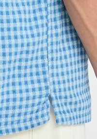 Cămașă cu model gingham în nuanțe de albastru deschis și alb, realizată dintr-un material texturat, cu slituri laterale la tiv pentru o potrivire relaxată.