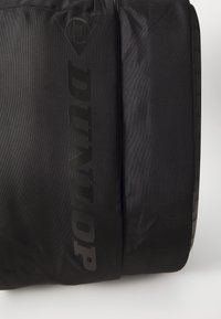 Schwarze Dunlop-Duffel-Tasche mit strukturiertem Finish, geprägtem Logo und kontrastierenden Materialien. Rechteckige Form mit verstärkten Akzenten.