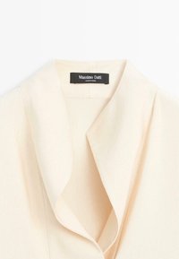 Roomkleurige, geribbelde blouse met een omslagkraag, voorzien van een label met de tekst "Massimo Dutti" en een gladde textuur over het geheel.