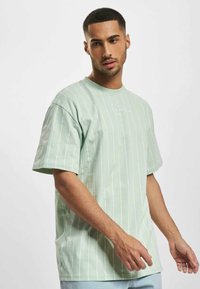 Lyst grænt bomulds t-shirt med lodrette hvide striber, rund halsudskæring og korte ærmer. Har et minimalistisk broderet logo på brystet.