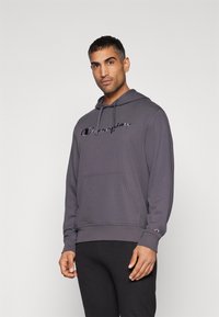 Sweatshirt à capuche gris avec une poche avant, des cordons de serrage et un logo brodé. Tissu texturé avec des poignets et un ourlet côtelés.