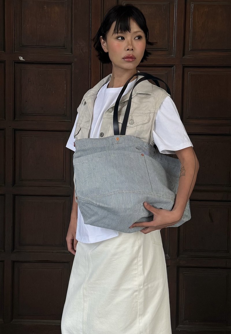 Ριγέ τσάντα ώμου φτιαγμένη από ύφασμα, με μαύρους ιμάντες, χαλαρή γραμμή και πορτοκαλί λεπτομέρειες. Φορεμένη από ένα άτομο σε casual ενδυμασία.