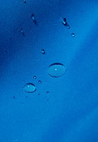 Bright blue fabric with a textured surface, featuring several water droplets resting on it, highlighting its water-resistant quality.