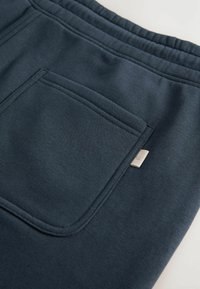 Pantalones de chándal azul marino oscuro con una textura suave, que cuentan con un bolsillo trasero y un pequeño acento de logo plateado en el lateral. Cintura elástica incluida.
