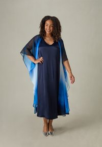 Dlouhé námořnické šaty s průhledným, ombre modrým pláštěm. Hladká látka, výstřih do V a široké rukávy. Modelka má na sobě stříbrné špičaté boty.
