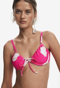 Roze bikini-top met ruches en bloemmotief. Voorzien van verstelbare bandjes en een gestrikt detail aan de voorkant. Soepele, rekbare stof.