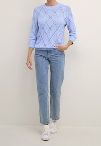 Jasnoniebieski sweter z dzianiny z diamentowymi wzorami, okrągłym dekoltem i rękawami o długości 3/4, zestawiony z jasnoniebieskimi dżinsami o prostym kroju i białymi sneakersami.