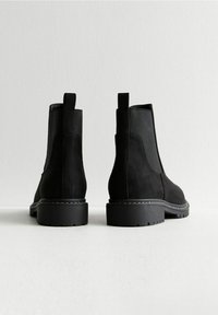 Black suede ankle boots with elastic side panels, sturdy rubber soles, and pull tabs at the back. Minimalist design with stitched detailing.