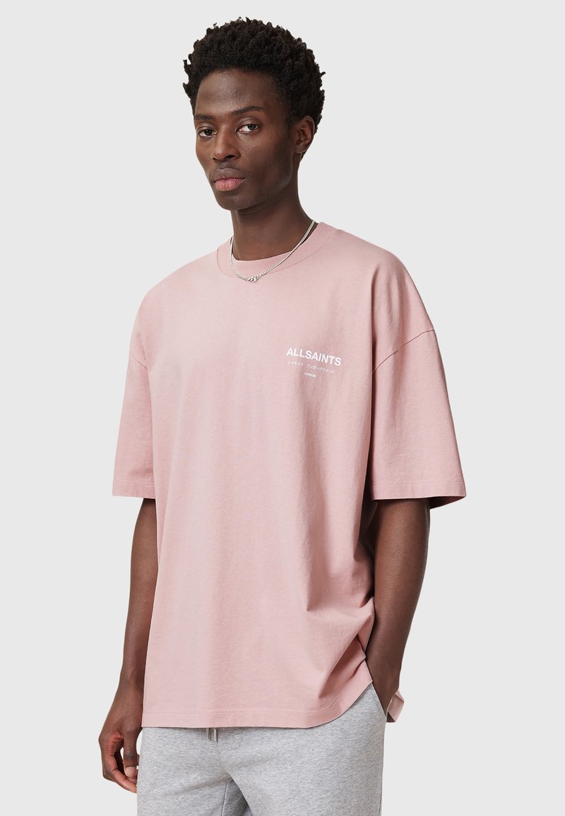 Camiseta de algodón de gran tamaño en color rosa empolvado, con mangas cortas y cuello redondo; cuenta con un pequeño logo blanco en el pecho.