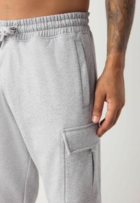 Graue Baumwoll-Sweatpants mit lockerer Passform, elastischem Bund und seitlicher Cargo-Tasche. Glatte Textur und minimale Nahtdetails.