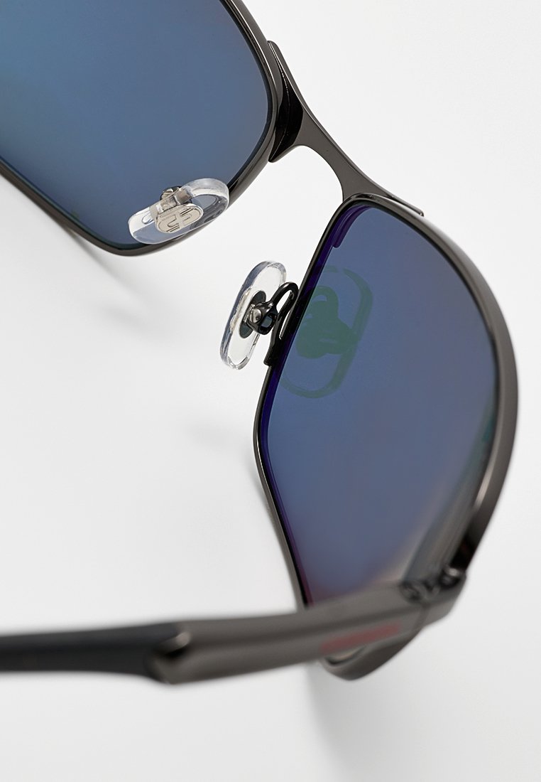 Lunettes de soleil noires avec des verres dégradés bleus, monture en métal et plaquettes de nez transparentes ajustables, présentant un design élégant et angulaire.