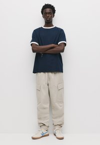 Marineblå bomulds T-shirt med hvid kant, parret med beige cargo bukser med lommer, og hvide sneakers med blå detaljer.