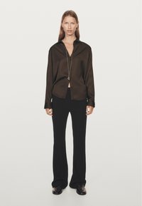 Dunkelbraune Seidenbluse mit Kragen, Knopfverschluss und langen Ärmeln, kombiniert mit schwarzen Schlaghosen und glänzenden schwarzen Schuhen.