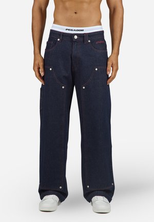 Dark blue denim trousers with a wide leg cut, featuring red stitching, multiple pockets, and metal snap accents. Includes a white waistband.