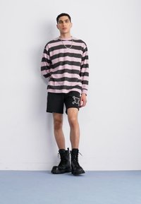 Camisa de manga larga a rayas en rosa y negro, combinada con pantalones cortos negros con un gráfico blanco, complementada con botas negras de cordones.