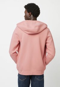 Lichtroze hoodie met een zachte textuur, geribde manchetten en zoom. Heeft een kangoeroezak en contrasterende stiksels.