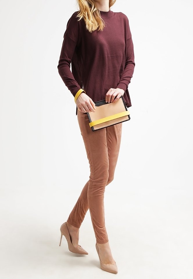 Burgundy långärmad topp, tighta beige byxor och beige klackar. Håller en flerfärgad väska med gula detaljer och svart kant.