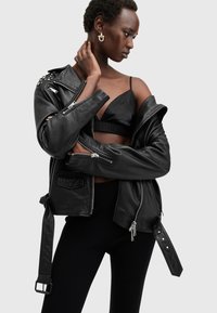 Black leather motorcycle jacket with silver hardware, zippered pockets, and studded accents. Model wears a black top and dark pants.