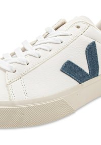 Baskets en cuir blanc avec un logo "V" en daim bleu bien visible, des lacets plats blancs et une semelle extérieure en caoutchouc texturée.