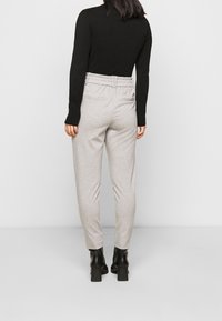 Lichtgrijze, elastische broek met een relaxte pasvorm, voorzien van twee achterzakken, gestyled met een aansluitend zwart langomtop en hoge laarzen.