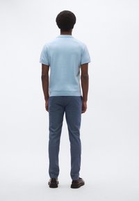 Ανοιχτό μπλε κοντομάνικο πόλο με γιακά, σε συνδυασμό με στενά σκούρα μπλε παντελόνια και μαύρα παπούτσια. Απλός σχεδιασμός και λεία υφή.