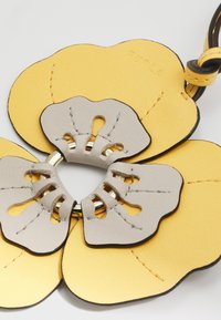 Accessoire floral en cuir avec des pétales jaunes et gris, présentant un anneau central en argent. Surfaces texturées et bords contrastés.