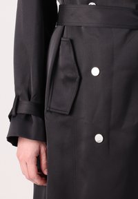 Cappotto nero con cintura in vita, tasche laterali e bottoni argentati. Tessuto morbido con un design classico e una vestibilità sartoriale.