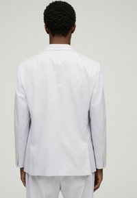 Light grey suit jacket made of smooth fabric. Features tailored design, straight cut, and gold button accents on the cuffs.