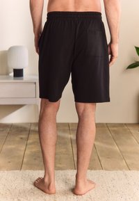 Pantalones cortos de algodón negros con cintura elástica, bolsillos laterales y un bolsillo trasero; textura suave, hasta la rodilla y diseño sencillo.