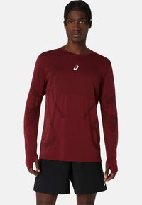 Langärmliges Sporthemd in tiefrot, mit einem subtilen Design, Rundhalsausschnitt und einem Logo auf der Brust. Der Stoff wirkt glatt und leicht.